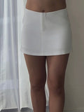 Person wearing a white skirt and white high-heeled shoes in a room with a curtain.